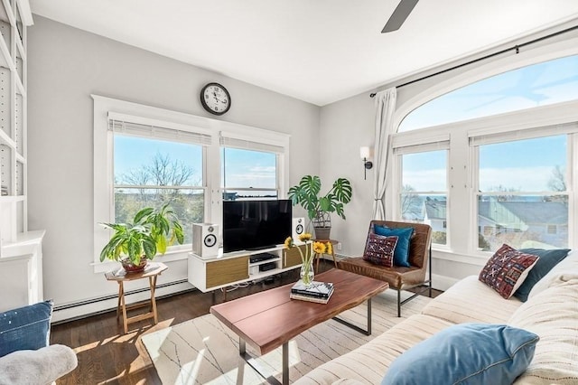 living area featuring plenty of natural light, a baseboard heating unit, a ceiling fan, and wood finished floors