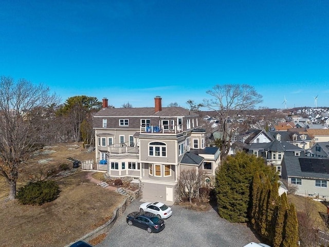 back of house with a residential view, a chimney, gravel driveway, and a balcony