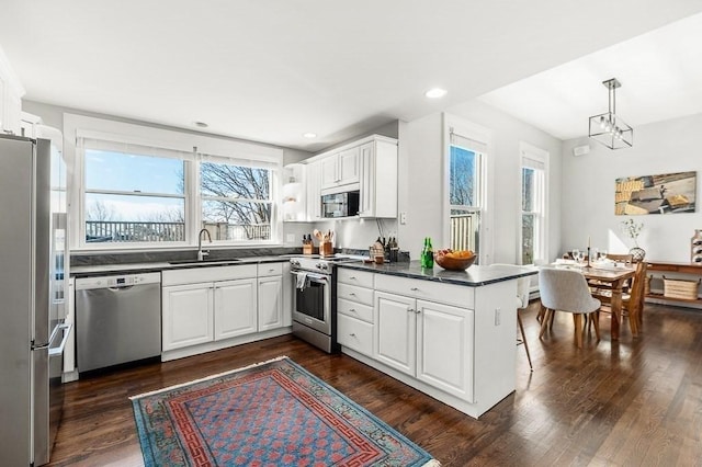 kitchen with a peninsula, a sink, stainless steel appliances, dark wood-type flooring, and dark countertops