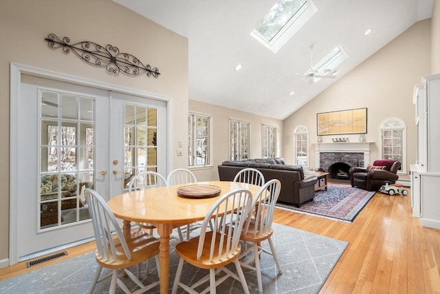 dining room with visible vents, light wood finished floors, a skylight, a fireplace, and french doors