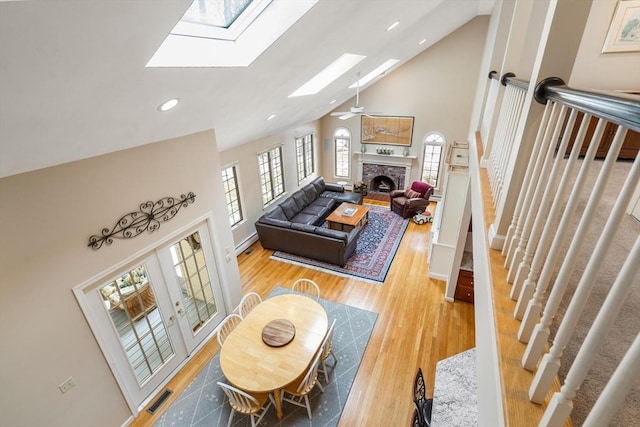 living room with light wood-type flooring, visible vents, high vaulted ceiling, a fireplace with raised hearth, and a skylight