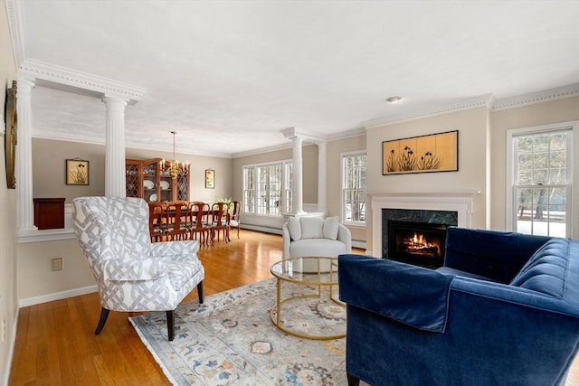 living area featuring a fireplace, wood finished floors, crown molding, and decorative columns