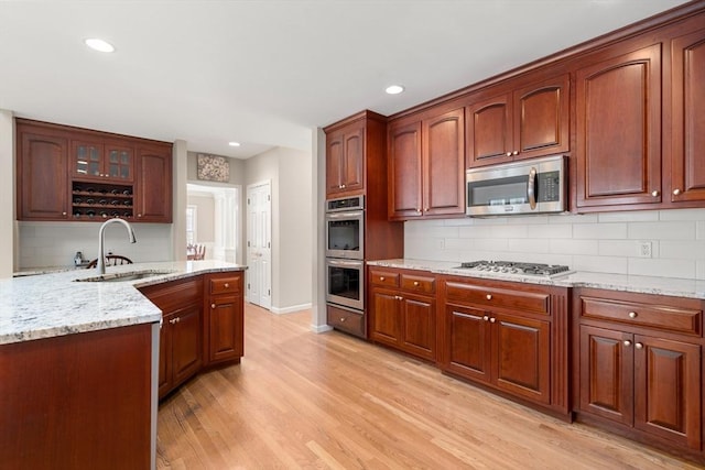 kitchen with glass insert cabinets, light stone counters, light wood-style flooring, stainless steel appliances, and a sink