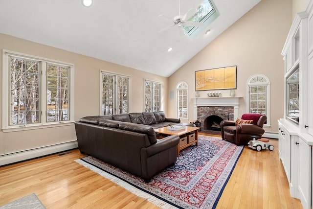 living area with a baseboard heating unit, a brick fireplace, a skylight, and light wood finished floors