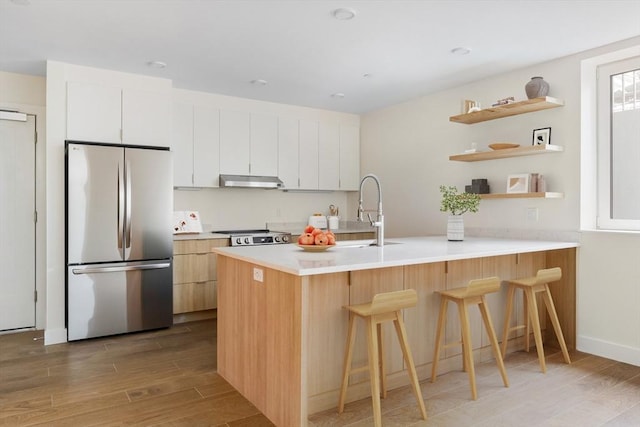 kitchen with stainless steel refrigerator, a kitchen breakfast bar, white cabinets, kitchen peninsula, and light wood-type flooring