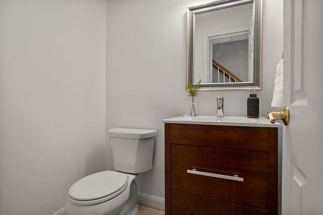 half bathroom with baseboards, vanity, and toilet