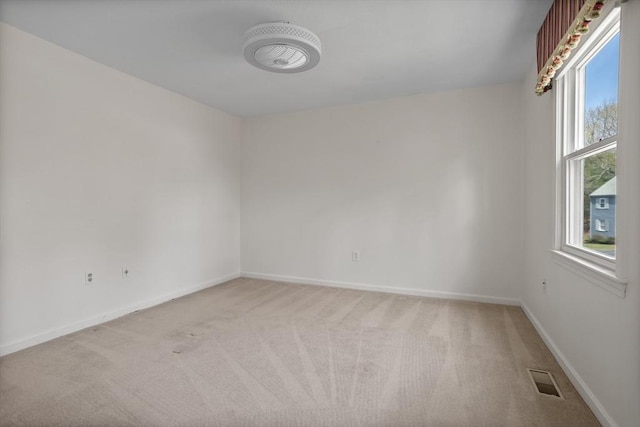 spare room featuring light colored carpet, baseboards, plenty of natural light, and visible vents