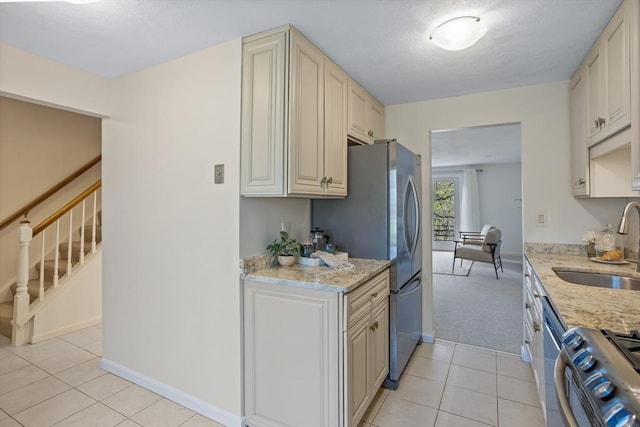 kitchen with light tile patterned flooring, cream cabinets, light stone counters, a sink, and appliances with stainless steel finishes
