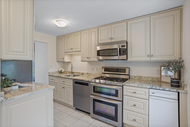 kitchen with cream cabinetry, appliances with stainless steel finishes, a sink, and light tile patterned floors