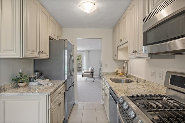 kitchen featuring stainless steel appliances, light stone countertops, light carpet, and a sink