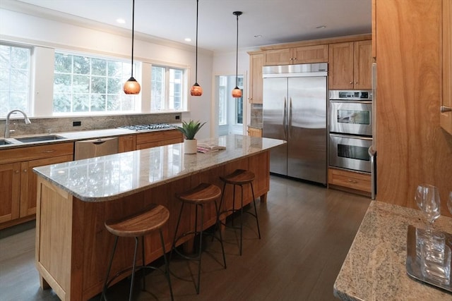 kitchen with dark wood-style floors, a kitchen island, light stone countertops, stainless steel appliances, and a sink