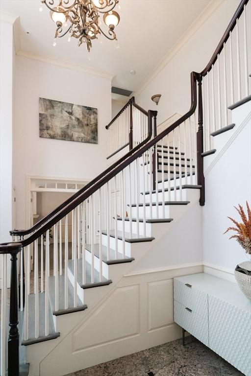 staircase with crown molding, a wainscoted wall, a decorative wall, and a notable chandelier