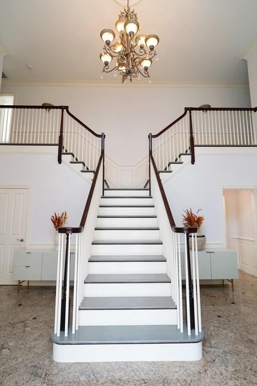 stairway with crown molding, a decorative wall, a high ceiling, and an inviting chandelier