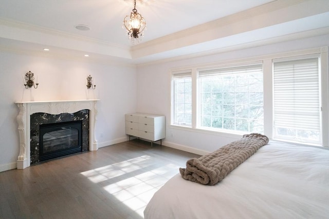 bedroom with baseboards, a raised ceiling, ornamental molding, wood finished floors, and a high end fireplace