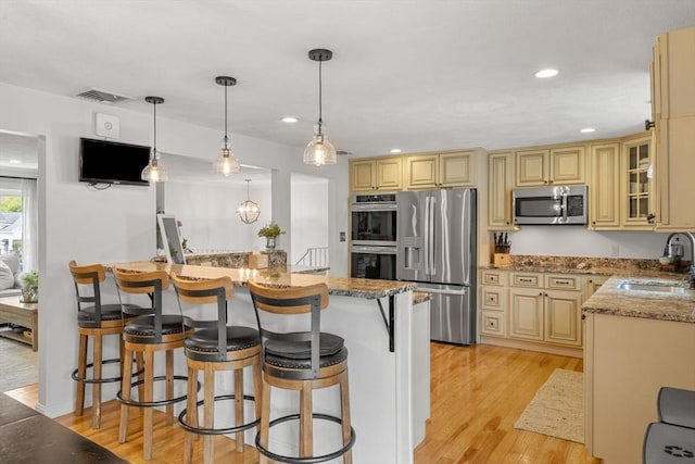 9 Indian Rock Dr, Saugus, MA 01906 - kitchen with stainless steel appliances, a sink, cream cabinets, a breakfast bar, and light wood-style flooring