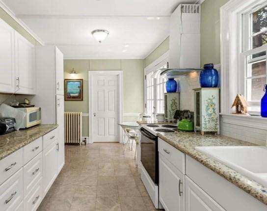 kitchen featuring radiator, white cabinets, wall chimney range hood, electric range, and light stone countertops