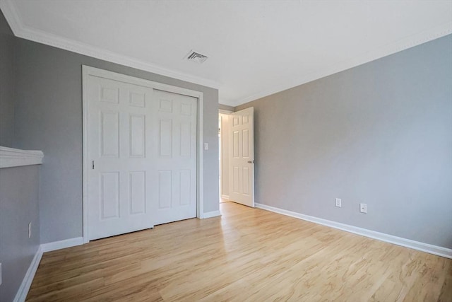 unfurnished bedroom with wood finished floors, baseboards, visible vents, ornamental molding, and a closet