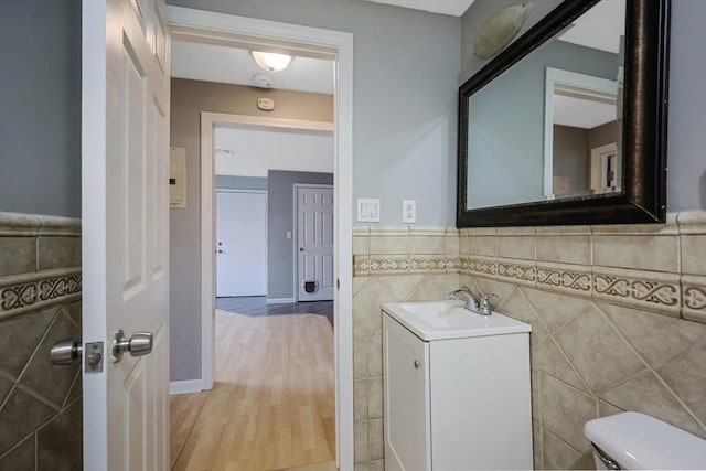 bathroom with toilet, tile walls, wainscoting, and vanity