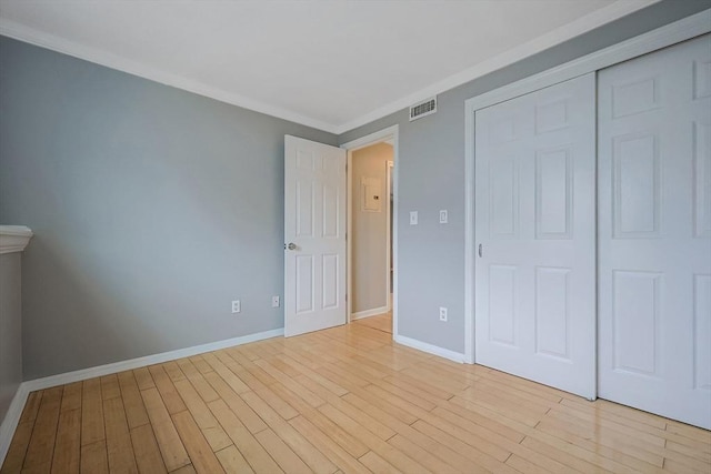 unfurnished bedroom with visible vents, a closet, light wood-style floors, crown molding, and baseboards