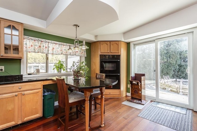 kitchen featuring pendant lighting, dark countertops, dobule oven black, glass insert cabinets, and wood finished floors