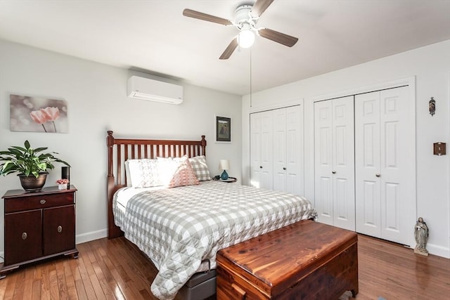 bedroom featuring multiple closets, a ceiling fan, an AC wall unit, baseboards, and hardwood / wood-style flooring