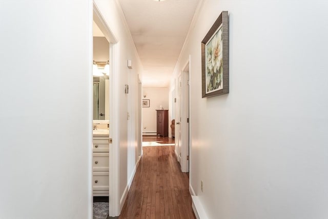 hall featuring dark wood-style floors, a sink, ornamental molding, and baseboards