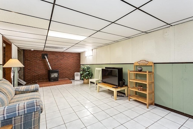 unfurnished living room with a wood stove, a drop ceiling, and light tile patterned flooring