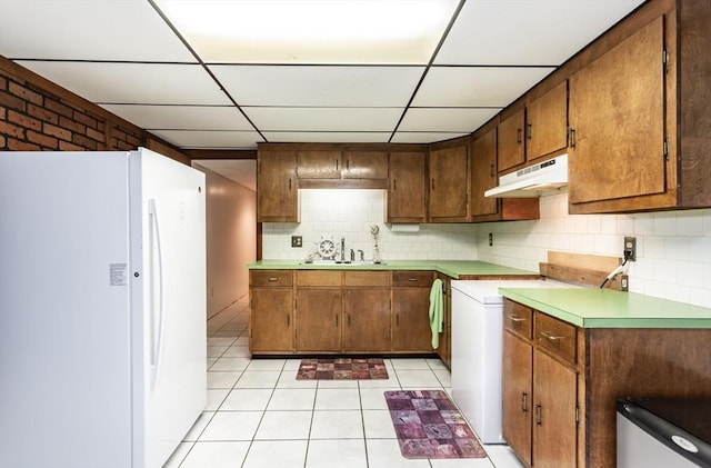 kitchen featuring tasteful backsplash, a drop ceiling, freestanding refrigerator, under cabinet range hood, and a sink