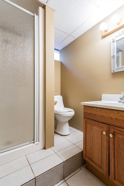 full bathroom with a stall shower, a drop ceiling, toilet, tile patterned flooring, and vanity