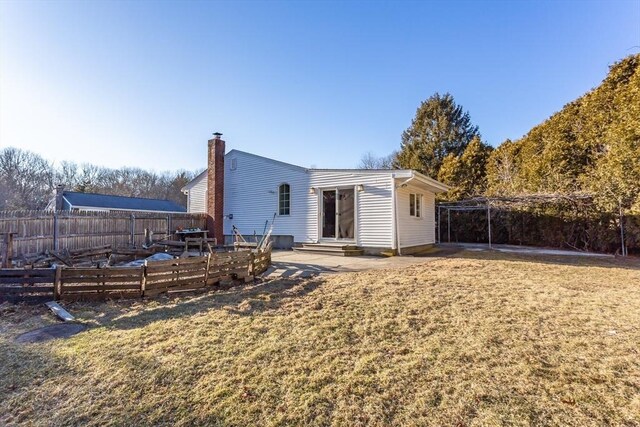 back of property featuring entry steps, a yard, a chimney, and fence