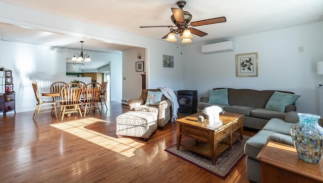 living room with ceiling fan with notable chandelier, a wall unit AC, wood finished floors, and a wood stove