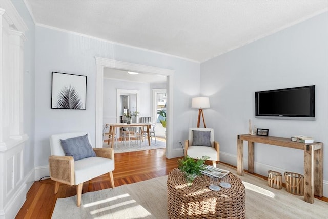 sitting room with decorative columns, hardwood / wood-style floors, and ornamental molding