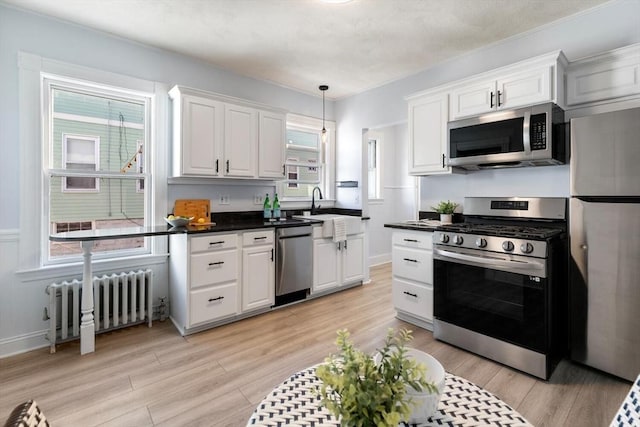 kitchen featuring radiator, white cabinets, light wood-type flooring, sink, and stainless steel appliances