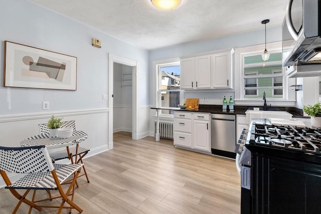 kitchen with white cabinetry, radiator, stainless steel appliances, and hanging light fixtures