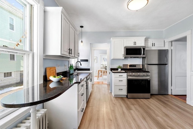 kitchen featuring white cabinets, light wood-type flooring, hanging light fixtures, and stainless steel appliances