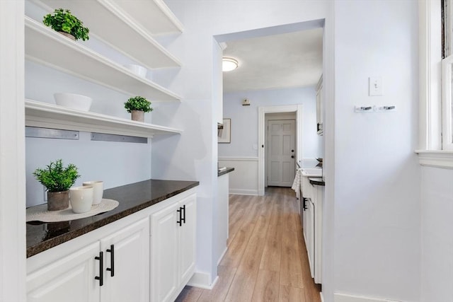 bar featuring light wood-type flooring, white cabinetry, and dark stone counters