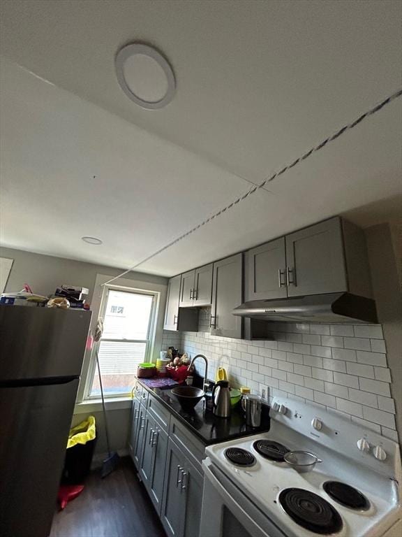 kitchen featuring gray cabinetry, white electric range oven, dark hardwood / wood-style floors, stainless steel fridge, and decorative backsplash