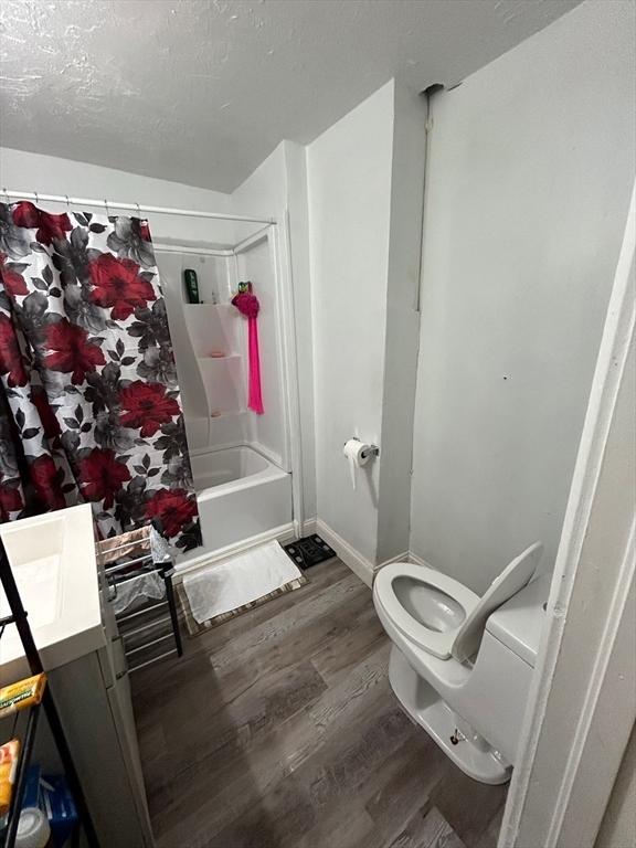 full bathroom featuring shower / tub combo, vanity, a textured ceiling, wood-type flooring, and toilet