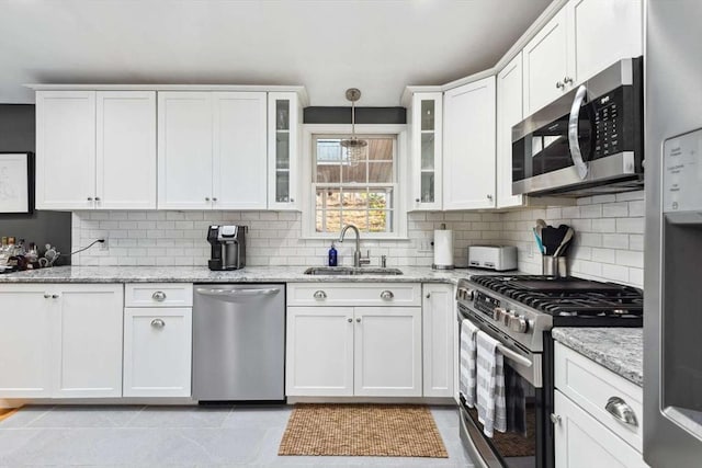 kitchen featuring decorative light fixtures, white cabinetry, stainless steel appliances, sink, and light stone counters