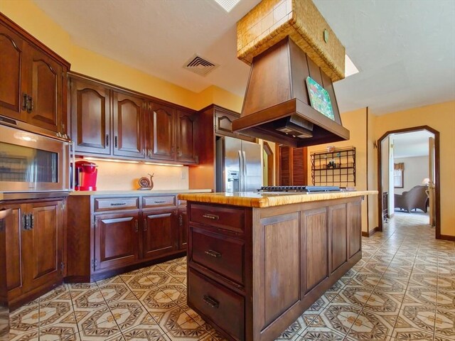 kitchen with a center island, light tile patterned floors, stainless steel appliances, and custom exhaust hood