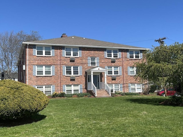 view of front facade featuring a chimney, brick siding, and a front yard