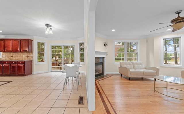 living room with a tiled fireplace, light tile patterned floors, ornamental molding, and ceiling fan