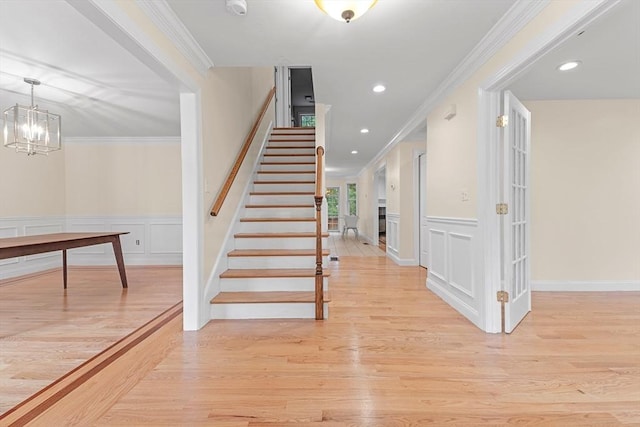 staircase featuring crown molding, wood-type flooring, and an inviting chandelier