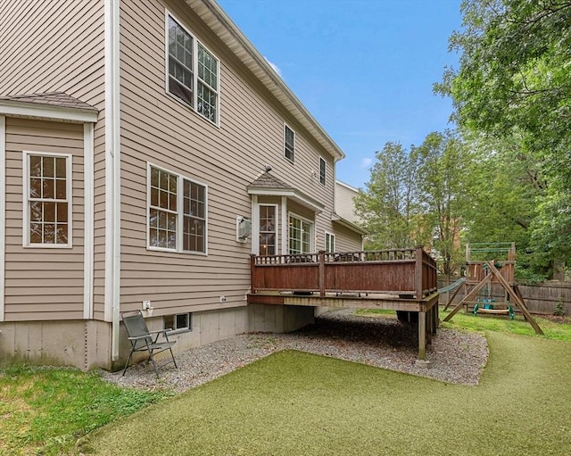 back of property featuring a wooden deck, a playground, and a lawn