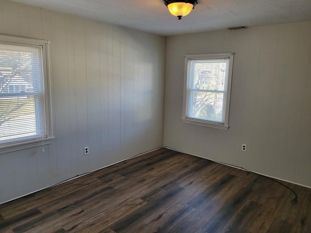 unfurnished room with dark wood-type flooring and wooden walls