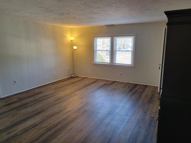 spare room featuring a textured ceiling, wooden walls, and dark wood-type flooring