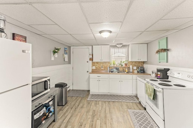 kitchen featuring sink, white appliances, light hardwood / wood-style floors, white cabinets, and a drop ceiling