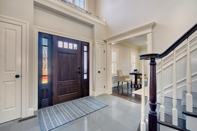 entrance foyer featuring visible vents, a high ceiling, crown molding, and stairway