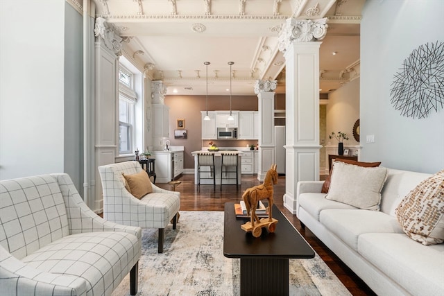 living room featuring decorative columns, beamed ceiling, hardwood / wood-style flooring, and sink