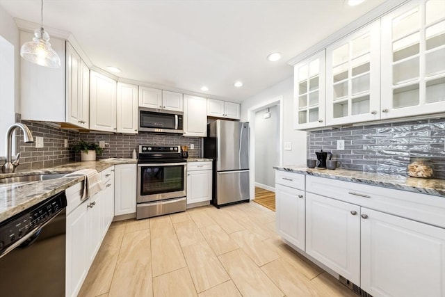 kitchen featuring pendant lighting, appliances with stainless steel finishes, white cabinetry, light stone countertops, and decorative backsplash